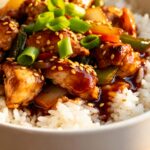 Bowl of Crockpot Teriyaki Chicken served over white rice, topped with sesame seeds and green onions.